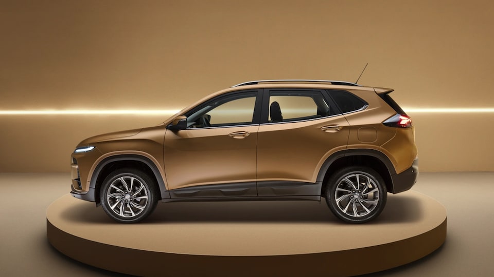 Vista lareral Tracker dourado exposto sobre plataforma circular, com fundo dourado iluminado por faixa de luz horizontal.