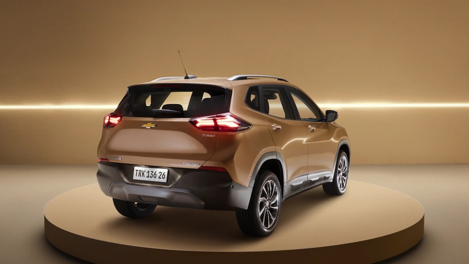 Vista traseira Tracker dourado exposto sobre plataforma circular, com fundo dourado iluminado por faixa de luz horizontal.