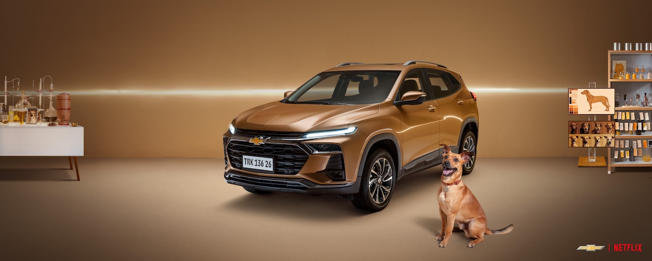 Tracker Caramelo em estúdio com fundo bege iluminado, acompanhado de um cachorro caramelo sentado à frente. Texto diz Tracker Caramelo – Dois ícones brasileiros em um lançamento especial!, com botões Saiba mais e Participar do leilão. Logotipos da Chevrolet e Netflix aparecem abaixo.