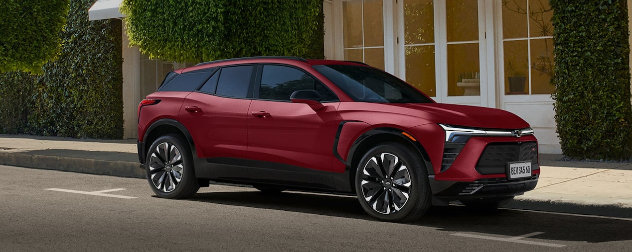 Chevrolet Blazer EV RS 2024 vermelho estacionado em frente a um prédio moderno com fachada verde, destaque para opção de assinatura mensal.