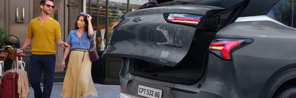 Chevrolet Captiva EV em foto ambientada. estacionado, com a tampa do porta-malas aberta, enquanto um casal se aproxima. Esta imagem ilustra a sessão de gerenciamento de carga da linha de acessórios originais Chevrolet.