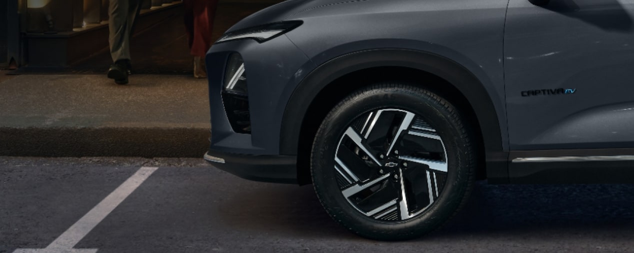 Chevrolet Captiva EV em foto ambientada. estacionado, com a tampa do porta-malas aberta, enquanto um casal se aproxima. Esta imagem ilustra a sessão de gerenciamento de carga da linha de acessórios originais Chevrolet.