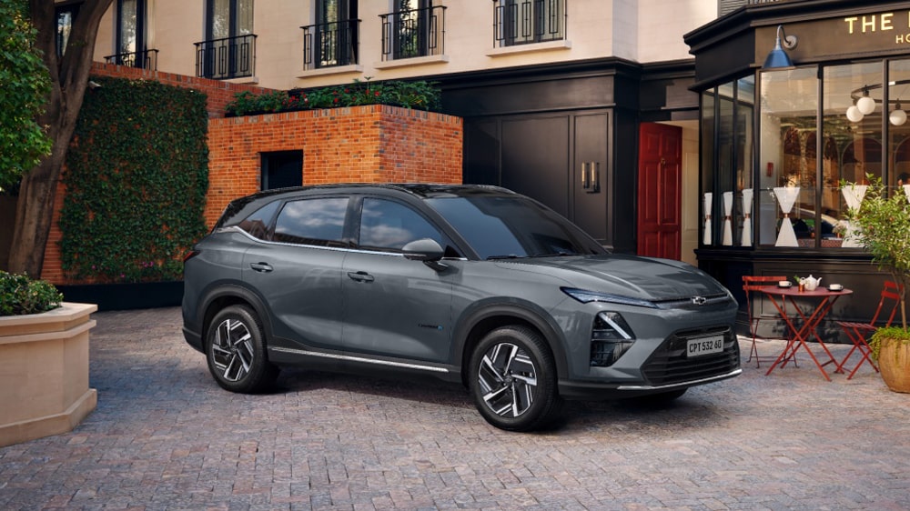 Chevrolet Captiva EV estacionado em frente a um café com mesas externas, em uma rua de paralelepípedos cercada por prédios elegantes.