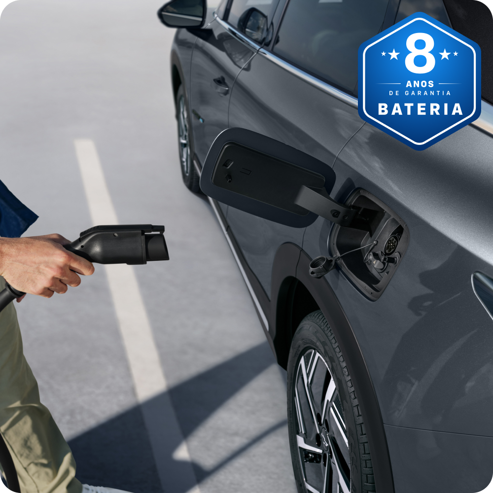 Pessoa conectando o cabo de carregamento em um SUV Chevrolet Captiva EV com selo azul indicando 8 anos de garantia da bateria.