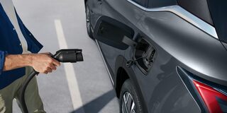 Pessoa conectando o cabo de carregamento em um SUV Chevrolet Captiva EV estacionado, mostrando o detalhe da porta de recarga elétrica.