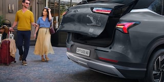 Casal caminhando com malas ao lado de um SUV Chevrolet Captiva EV, com o porta-malas aberto em frente a um edifício elegante.