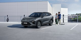 Casal ao lado de um SUV Chevrolet Captiva EV cinza estacionado em um ponto de recarga elétrica em área aberta e moderna.