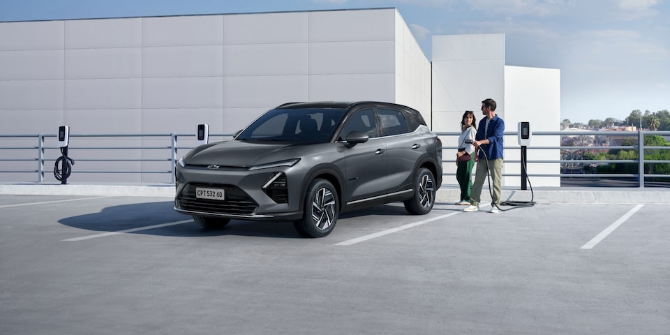 Casal ao lado de um SUV Chevrolet Captiva EV cinza estacionado em um ponto de recarga elétrica em área aberta e moderna.