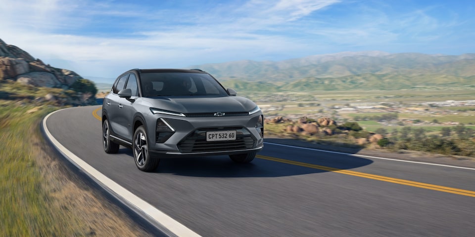 Chevrolet Captiva EV em movimento em uma estrada sinuosa cercada por montanhas e vegetação sob céu azul.