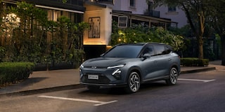 Chevrolet Captiva EV estacionado em uma rua urbana arborizada, com fachada iluminada de restaurante ou hotel ao fundo.