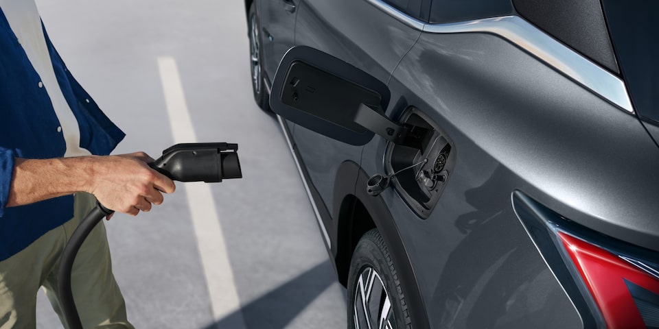 Pessoa conectando o cabo de carregamento em um SUV Chevrolet Captiva EV estacionado, mostrando o detalhe da porta de recarga elétrica.