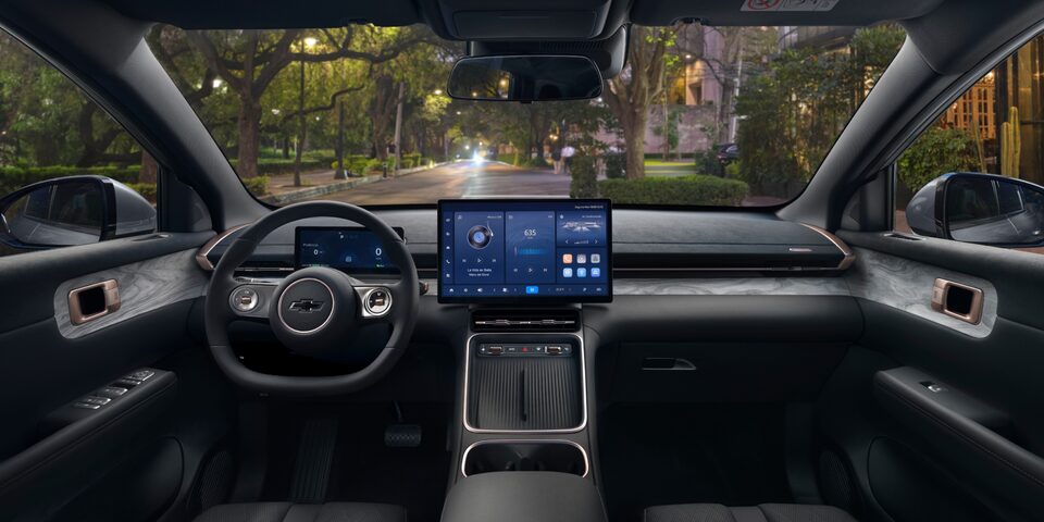 Interior do SUV Chevrolet Captiva EV, mostrando o volante com o logotipo da Chevrolet e o painel digital com duas telas grandes de comando e entretenimento.
