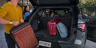 Pessoa colocando malas no porta-malas aberto de um SUV Chevrolet Captiva EV, com outras pessoas ao fundo se preparando para viajar.