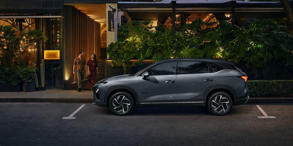 Chevrolet Captiva EV estacionado em frente a um restaurante iluminado, com um casal saindo do local à noite.