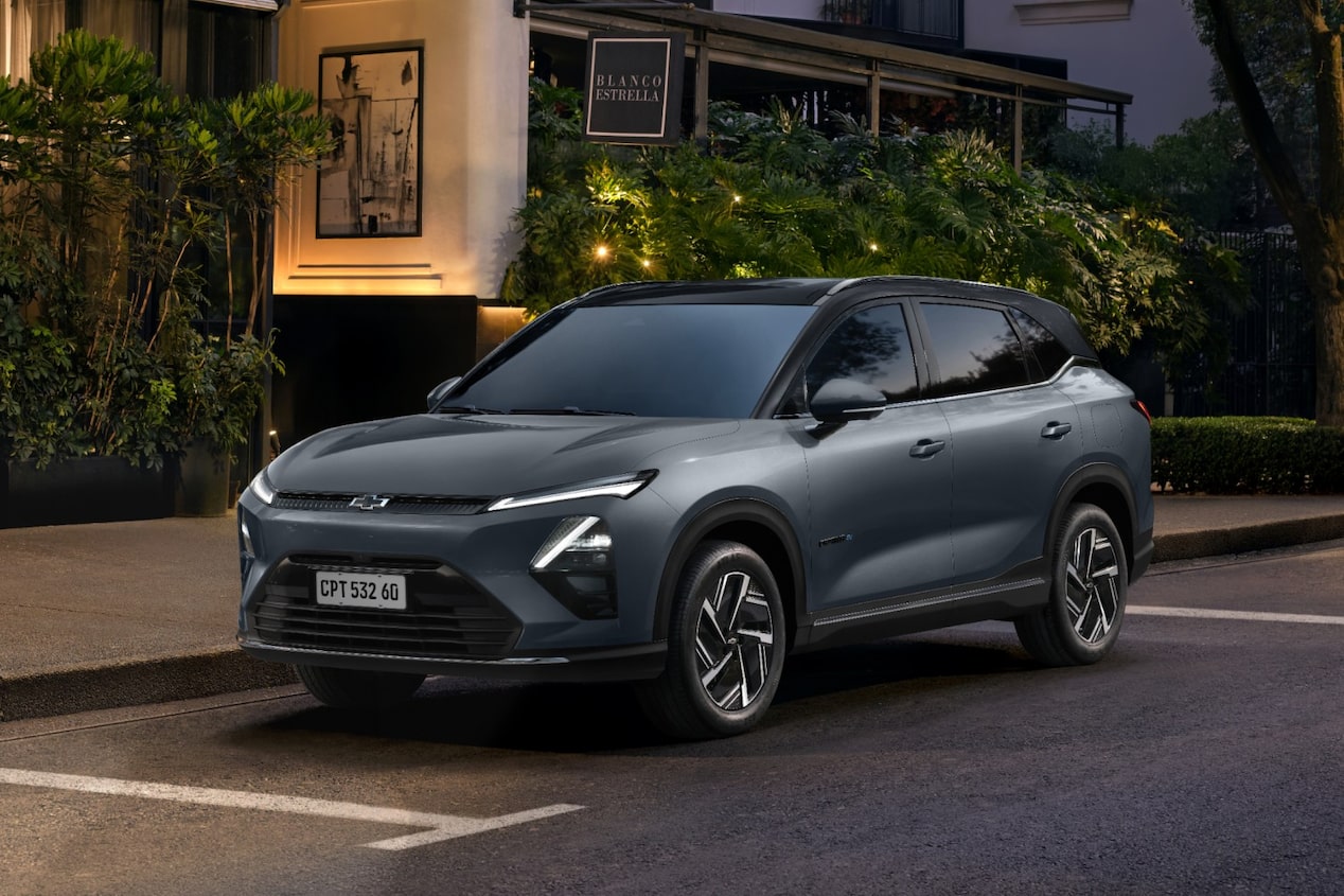 Chevrolet Captiva EV estacionado em uma rua urbana arborizada, com fachada iluminada de restaurante ou hotel ao fundo.