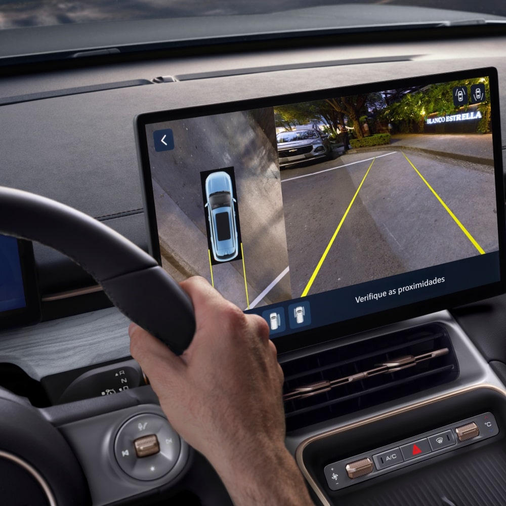 Condutor ao volante de um SUV Chevrolet Captiva EV, com a tela central exibindo o sistema de câmeras de ré e visão 360 graus para auxílio de estacionamento.