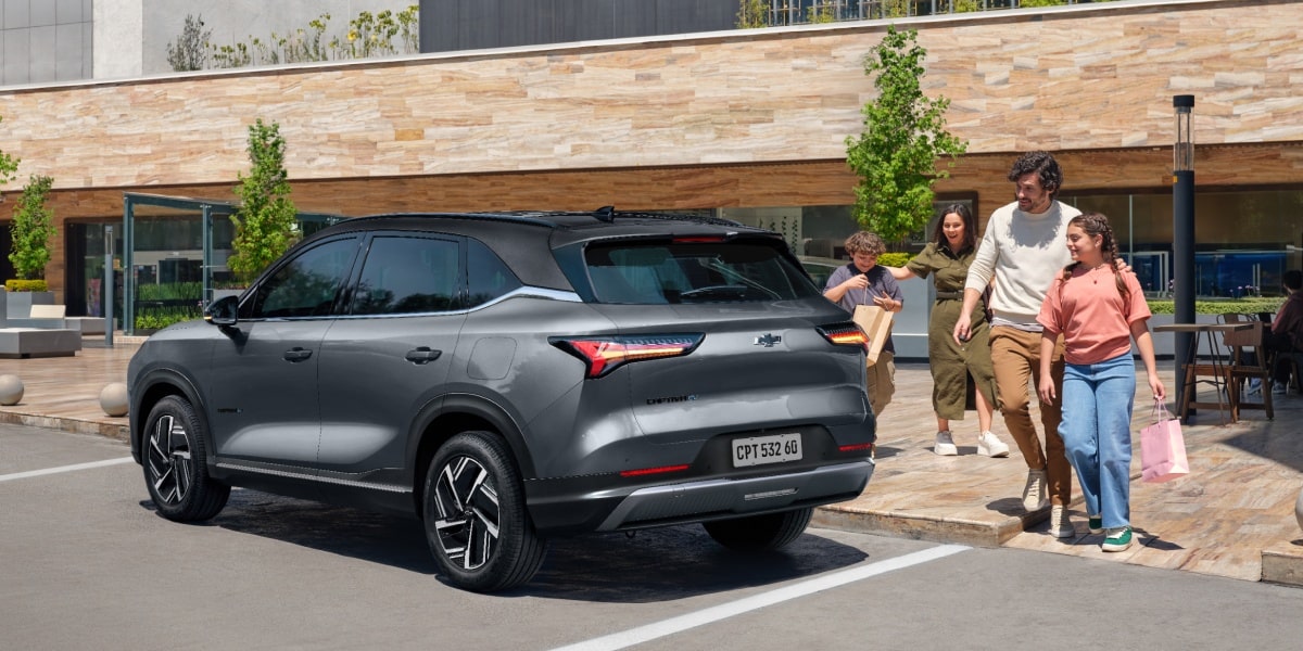 Família caminhando sorridente em direção a um SUV Chevrolet Captiva EV estacionado em frente a um prédio moderno com fachada de pedra.