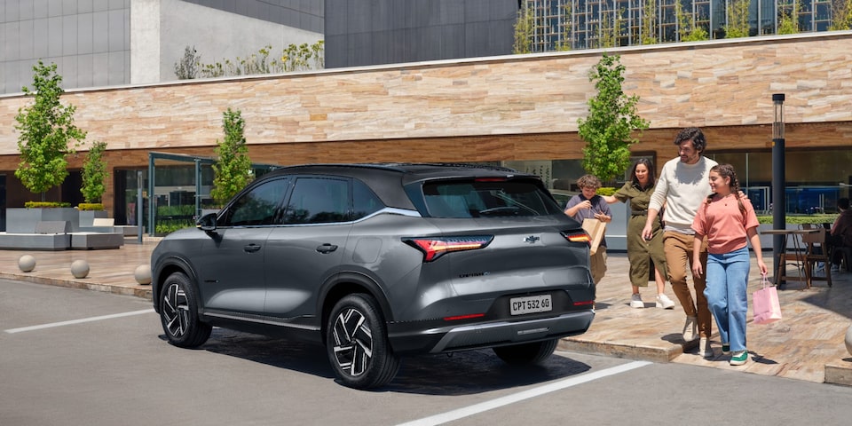 Família caminhando sorridente em direção a um SUV Chevrolet Captiva EV estacionado em frente a um prédio moderno com fachada de pedra.
