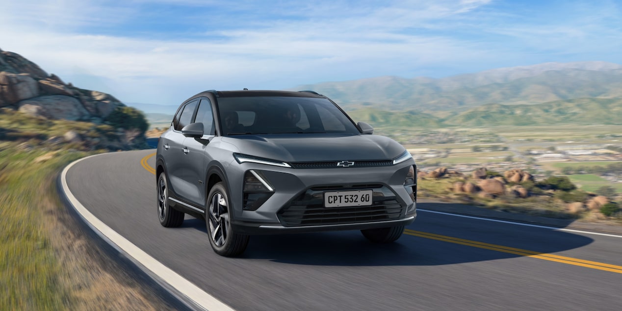 Chevrolet Captiva SUV Elétrico cinza escuro, em uma estrada panorâmica, com montanhas e paisagem urbana ao fundo sob céu azul.