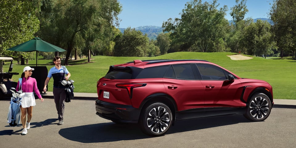Casal saindo de um carro elétrico Chevrolet com bolsas de golfe
