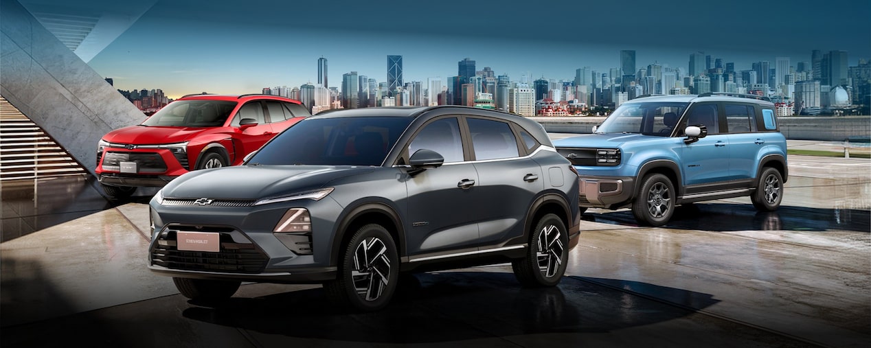 Chevrolet Equinox EV em primeiro plano, com Chevrolet Blazer EV vermelho e Chevrolet Spark elétrico Azul Atlântico ao fundo em ambiente urbano.