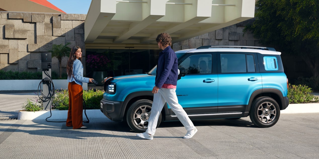 Chevrolet Spark azul estacionado em frente a uma edificação, com duas pessoas próximas ao veículo.