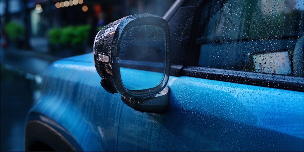 Close do retrovisor do Spark EUV Azul Atlântico com gotas de chuva, destacando o acabamento lateral em um dia chuvoso.