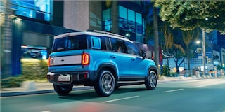 Spark EUV Azul Atlântico em movimento em avenida urbana, com prédios espelhados ao fundo.