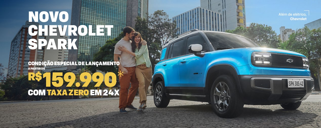 Banner de lançamento do Chevrolet Spark EV visto de frente e lateral direita, estacionado em avenida urbana com prédios altos ao fundo. À esquerda, texto promocional: Novo Chevrolet Spark – condição especial de lançamento a partir de R$ 159.990 com taxa zero em 24x. À frente do carro, um casal sorridente se abraça. No canto superior direito, slogan Além de elétrico, Chevrolet.