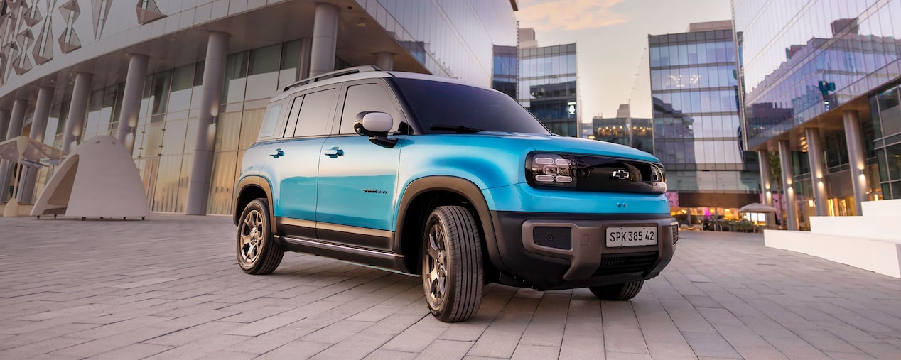 Spark EUV azul atlântico estacionado em área urbana moderna, cercado por prédios espelhados e iluminação suave do entardecer.