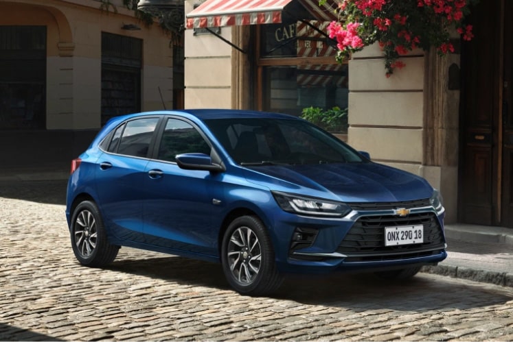 Onix estacionado em rua de paralelepípedo com flores ao fundo