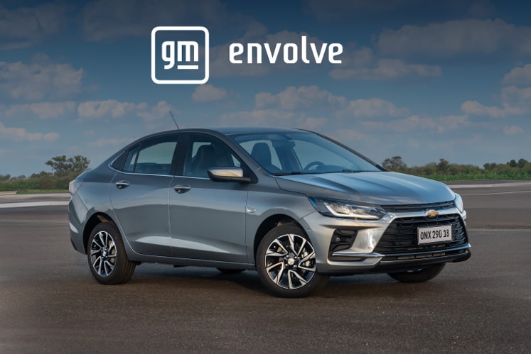Imagem do Onix Plus com logotipo GM Envolve sobreposto, estacionado em ambiente externo.