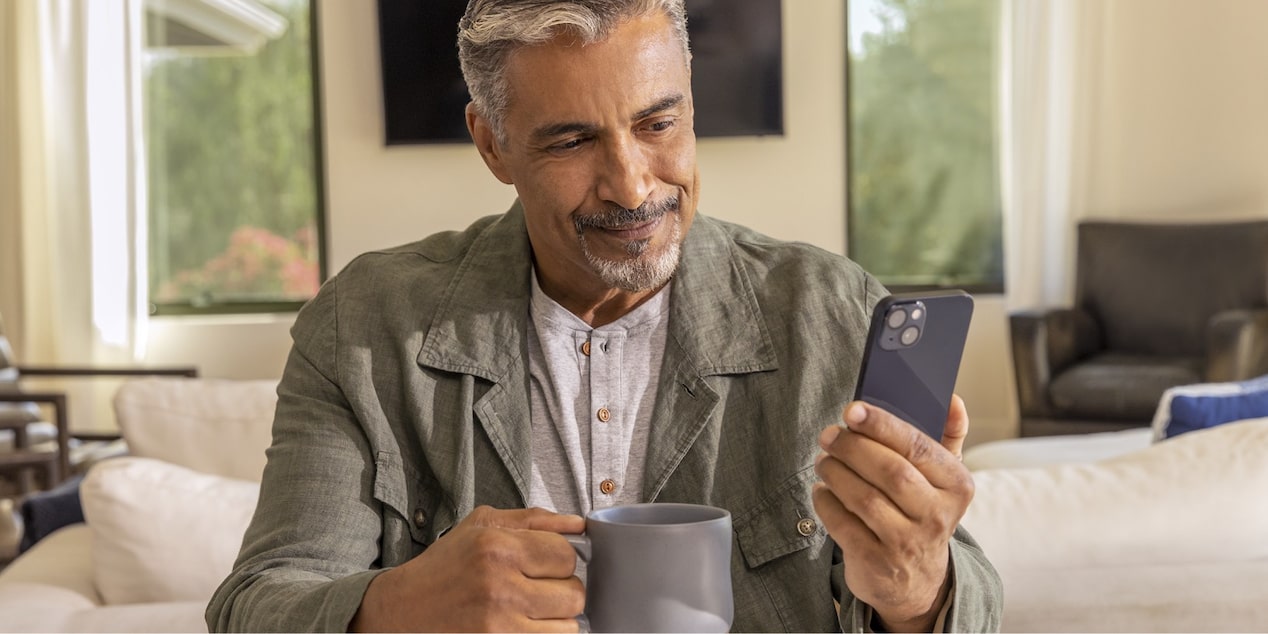 Homem com um celular e uma xícara na mão