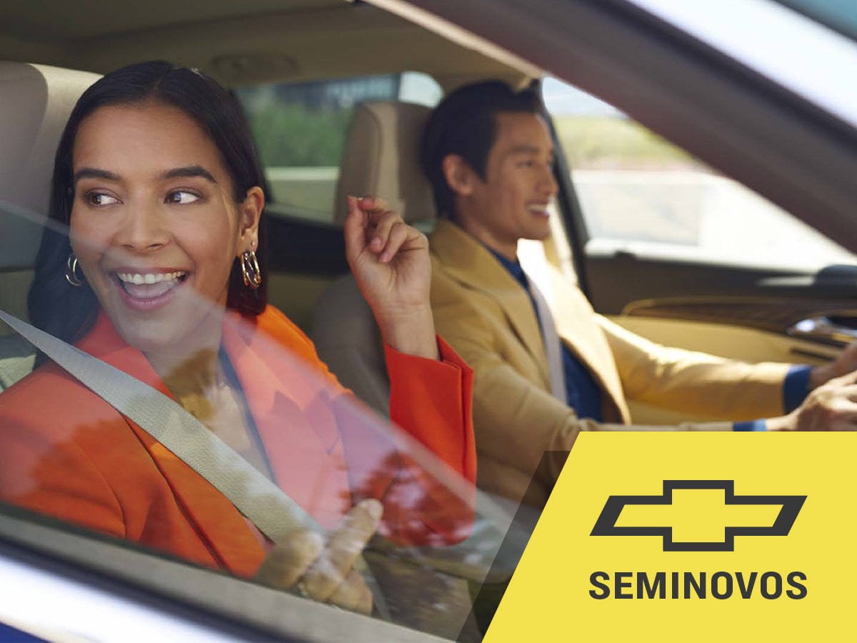 Casal sorridente dentro de um Chevrolet, com a mulher no banco do passageiro.