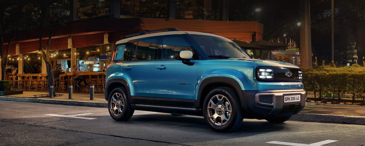 Spark EV azul estacionado em um posto de recarga à noite, com iluminação amarela e vegetação ao fundo. Texto sobreposto: Recarregue as energias agora mesmo.