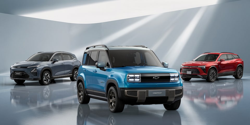 Alt Quatro SUVs modernos - Equinox EV, Blazer EV, Captiva EV e Spark EV - estão estacionados em um ambiente interno minimalista e bem iluminado, com paredes brancas e feixes de luz.
