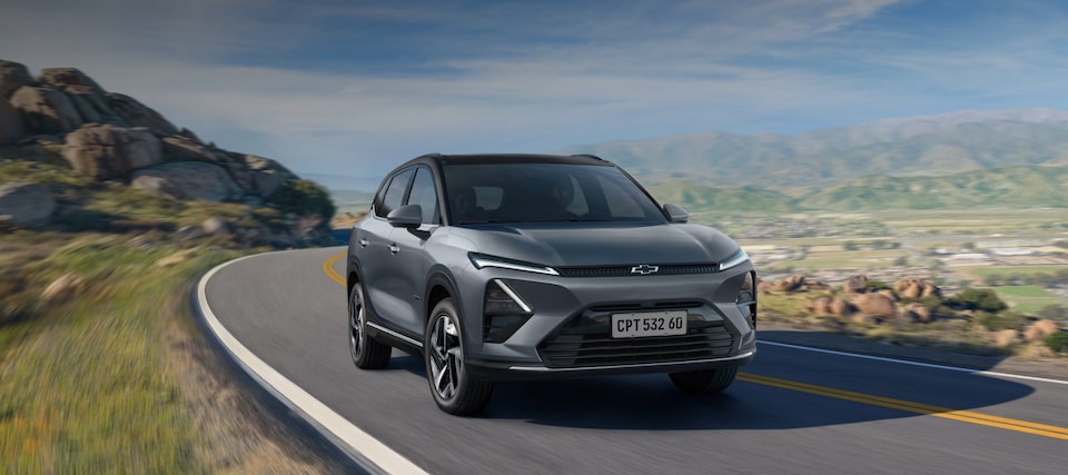 Chevrolet Captiva EV em movimento em uma estrada sinuosa cercada por montanhas e vegetação sob céu azul.