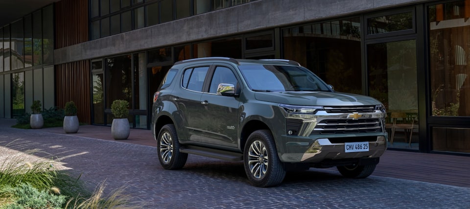 Um SUV Equinox Chevrolet vermelho está estacionado em uma entrada de pedra em frente a uma casa com portas de garagem brancas e paisagismo.
