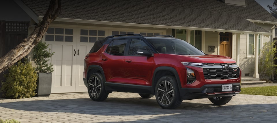 Um SUV Equinox Chevrolet vermelho está estacionado em uma entrada de pedra em frente a uma casa com portas de garagem brancas e paisagismo.