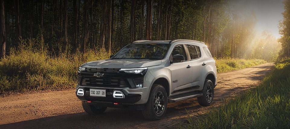 Chevrolet Trailblazer High Country Midnight Edition estacionado em um ambiente externo e em uma estrada de terra. Ao fundo, temos arbustos, plantas e árvores e o Sol de fim de tarde ilumina o carro.