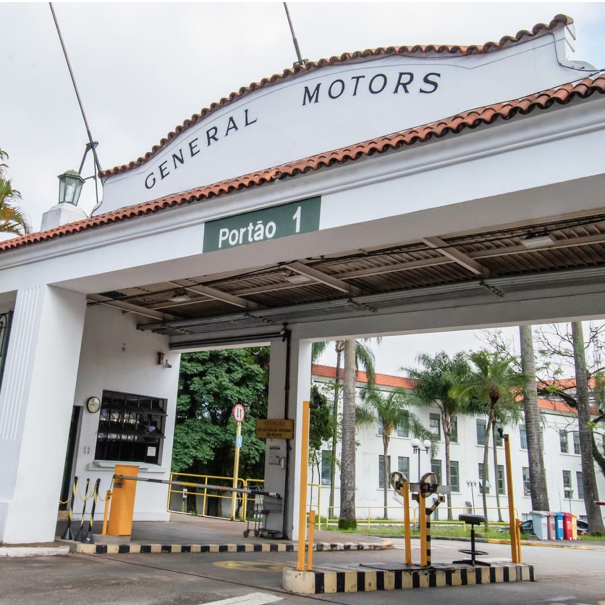Entrada principal da fábrica da General Motors em São Caetano do Sul, com portão branco identificado como Portão 1 e letreiro General Motors no topo.