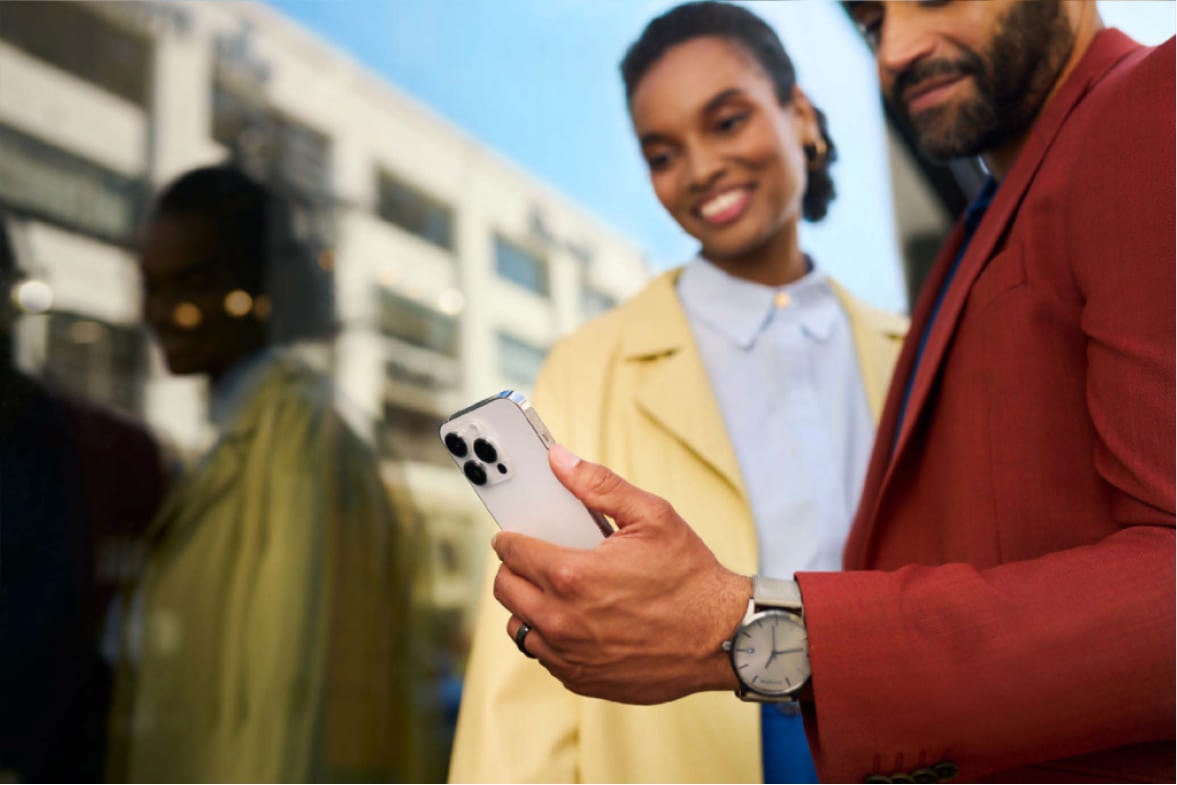 um casal, um homem com um blazer vermelho e uma mulher com camisa branca e jaqueta amarela, estão usando o app myChevrolet no smartphone.