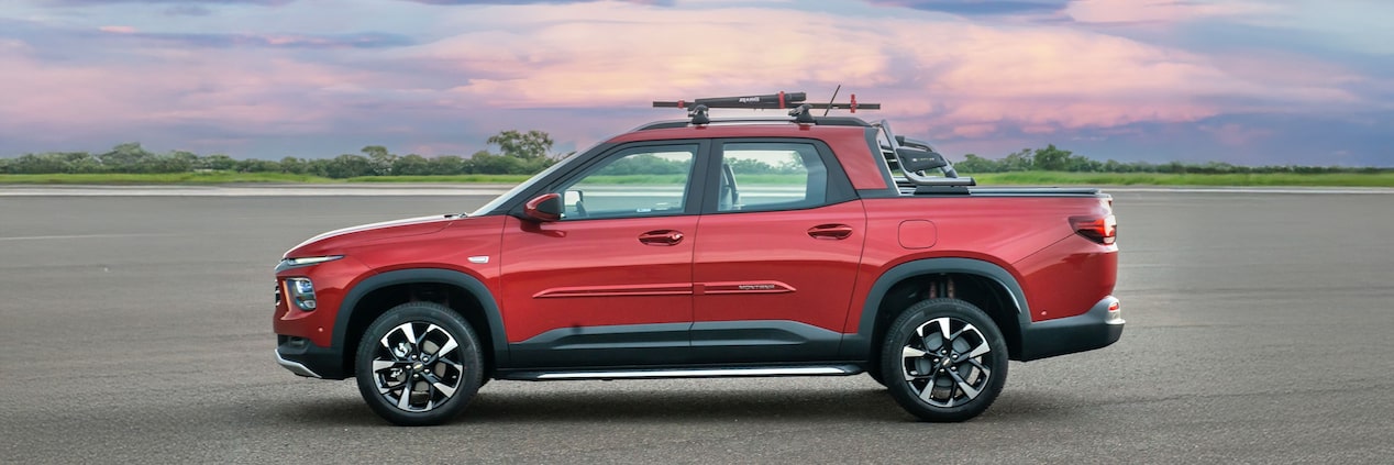 Chevrolet Montana vermelha em foto ambientada, estacionada a céu aberto, em visão lateral.