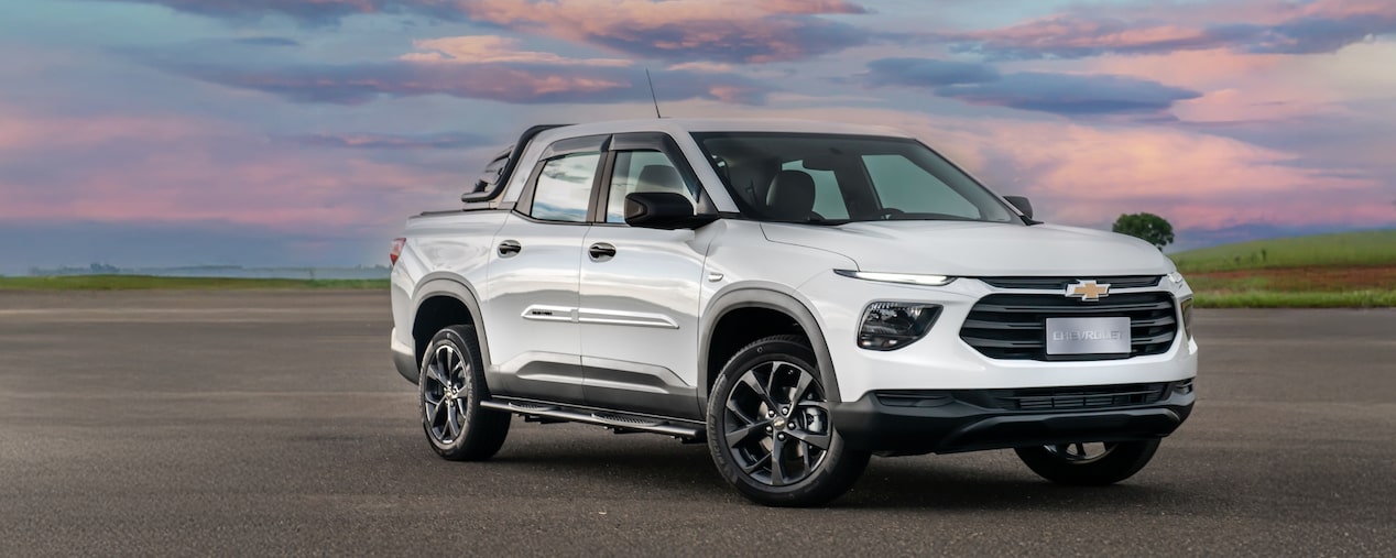 Chevrolet Montana branca em imagem ambientada, estacionada a céu aberto, em posição 3/4 de frente.