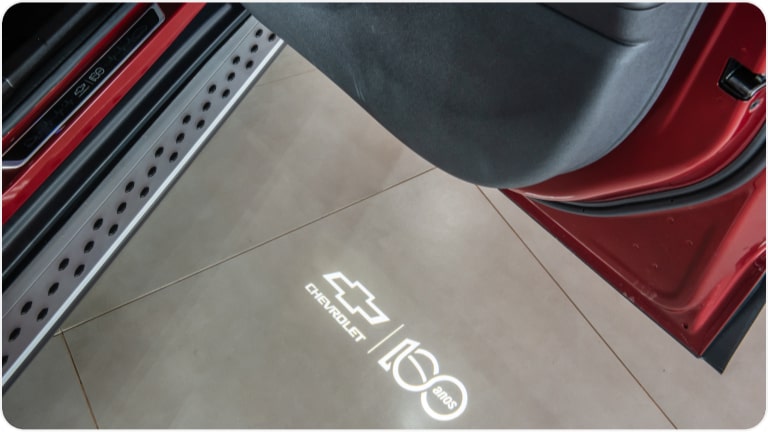 Luz de cortesia com logo Chevrolet 100 anos da linha de acessórios originais Chevrolet para a picape Montana.