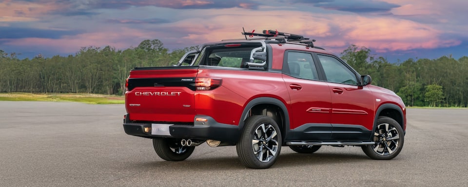 Chevrolet Montana vermelha em imagem ambientada, estacionada a céu aberto, em posição 3/4 de costas.