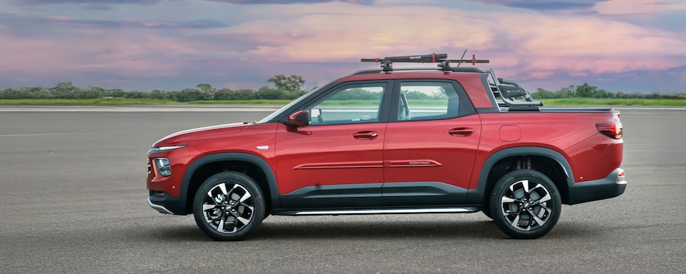 Chevrolet Montana vermelha em foto ambientada, estacionada a céu aberto, em visão lateral.