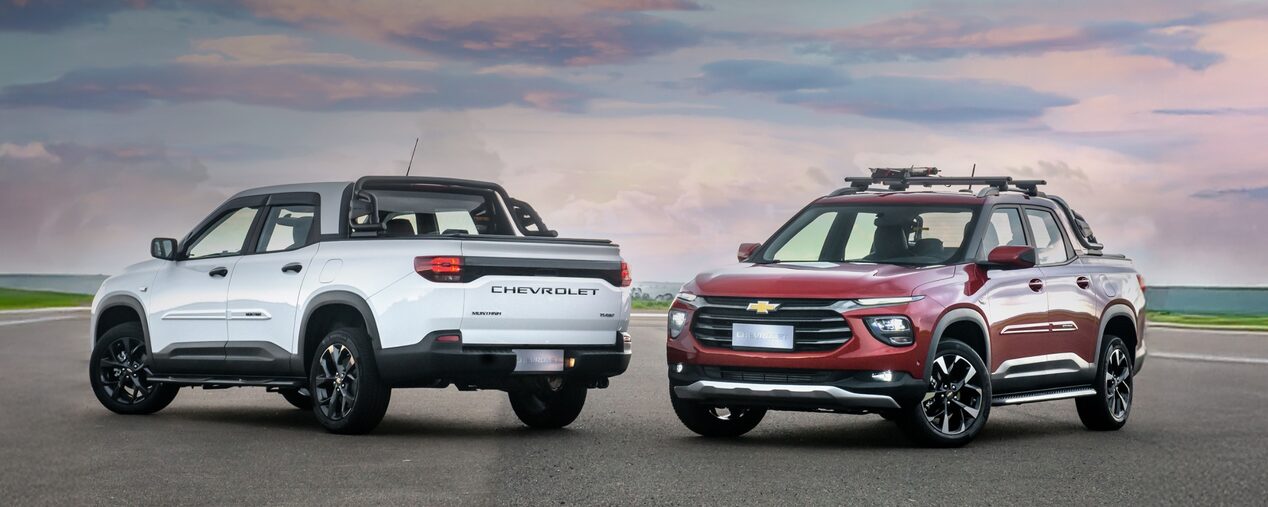 Chevrolet Montana branca e Chevrolet Montana vermelha em foto ambientada, estacionadas uma de frente para a outra a céu aberto. No quadrante superior esquerdo, o texto: Montana - acessórios universais.