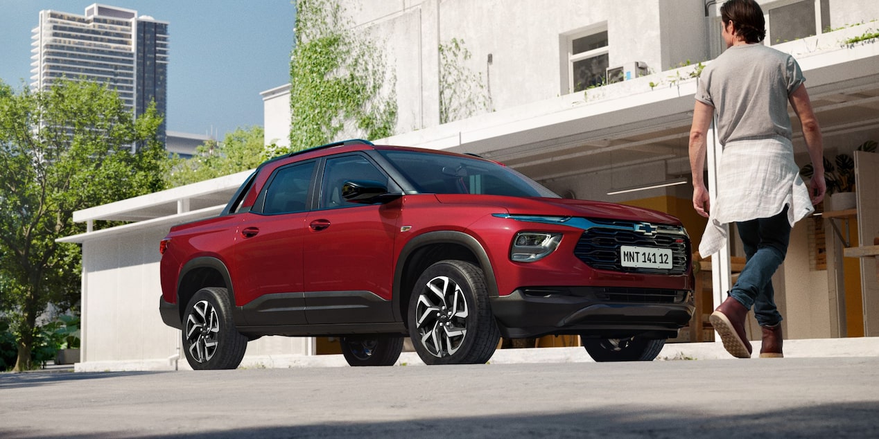 Chevrolet Montana na cor Vermelho Scarlet estacionada em frente a prédio urbano moderno com homem caminhando ao fundo