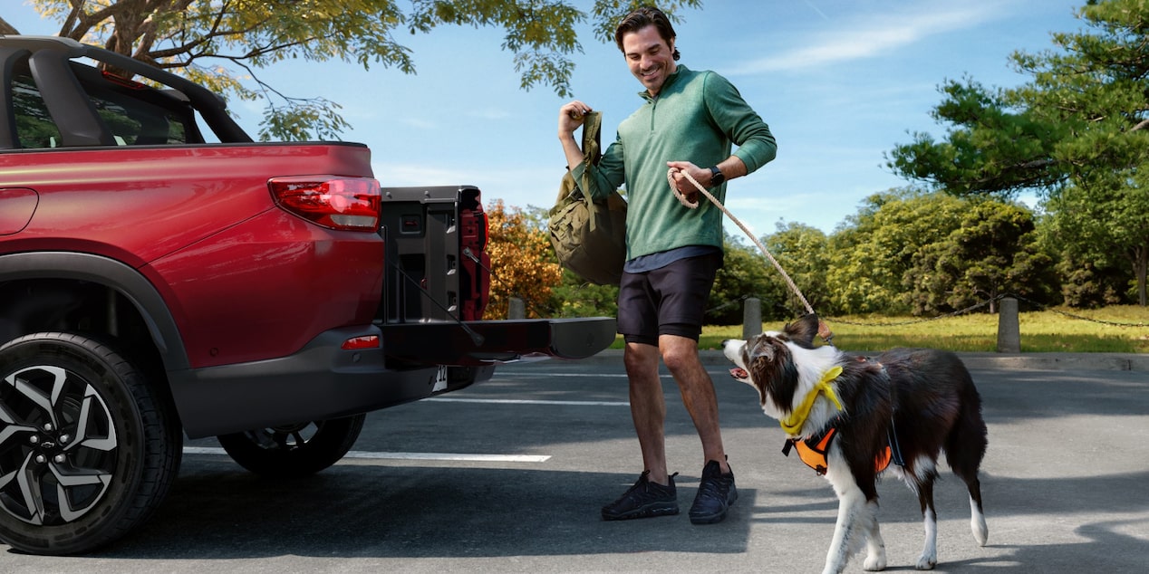 Homem sorridente com dois cachorros interagindo com a caçamba aberta da Chevrolet Montana na cor Vermelho Scarlet, em ambiente externo arborizado